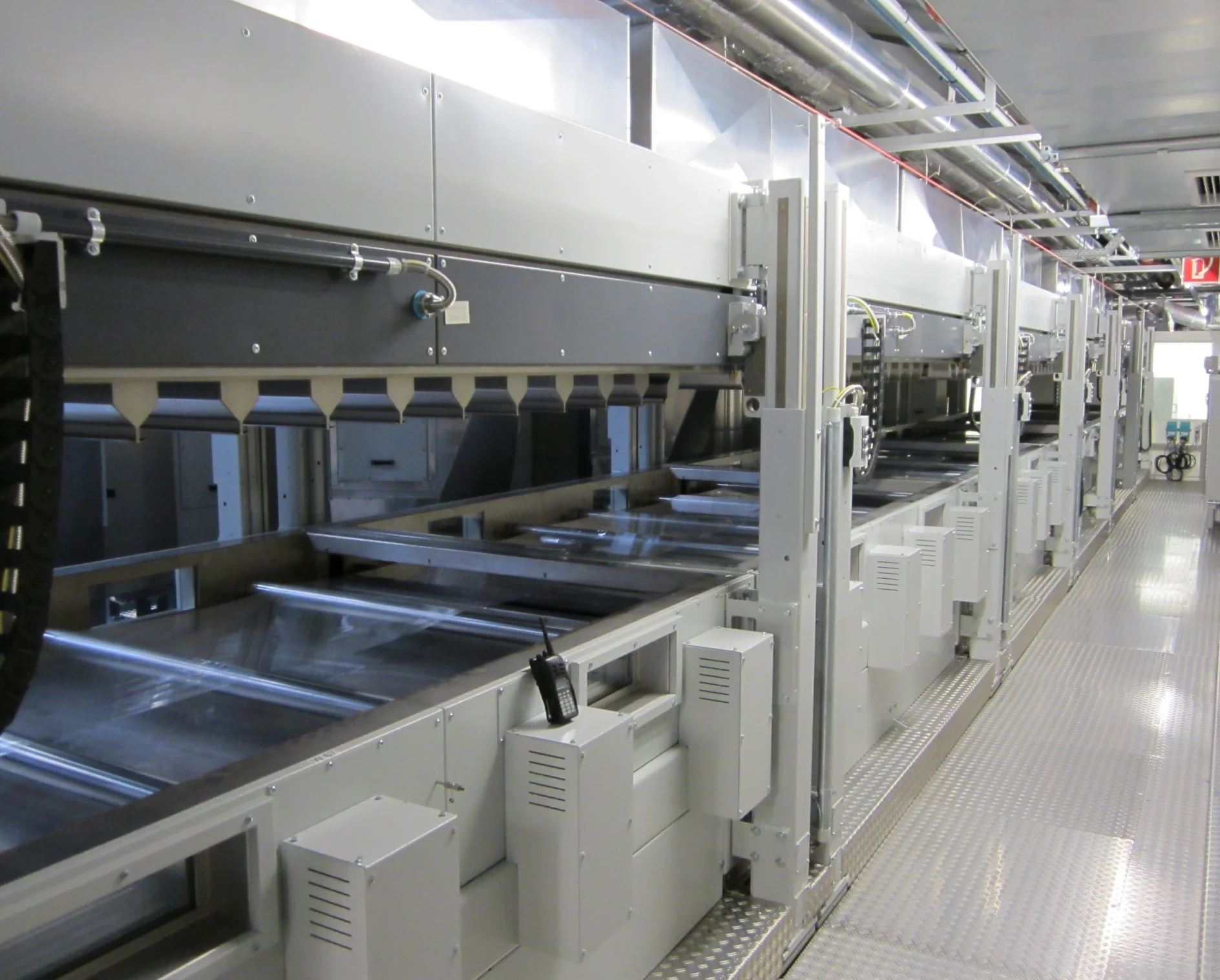 A large industrial machine with metal trays and conveyor system, featuring tesa tape dispensers inside a bright, clean facility. (This text has been generated by AI)