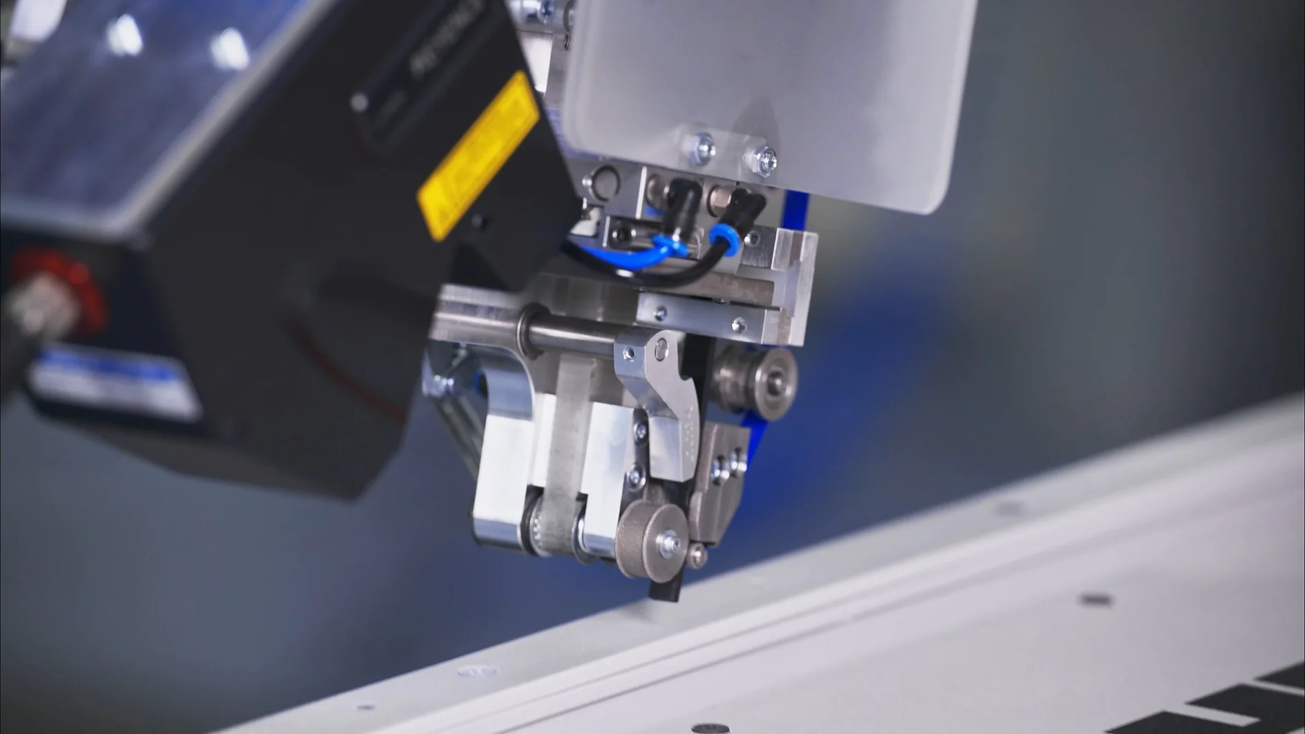 Close-up of an industrial robotic arm with mechanical components, wires, and tesa tape above a white surface, suggesting automation. (This text has been generated by AI)