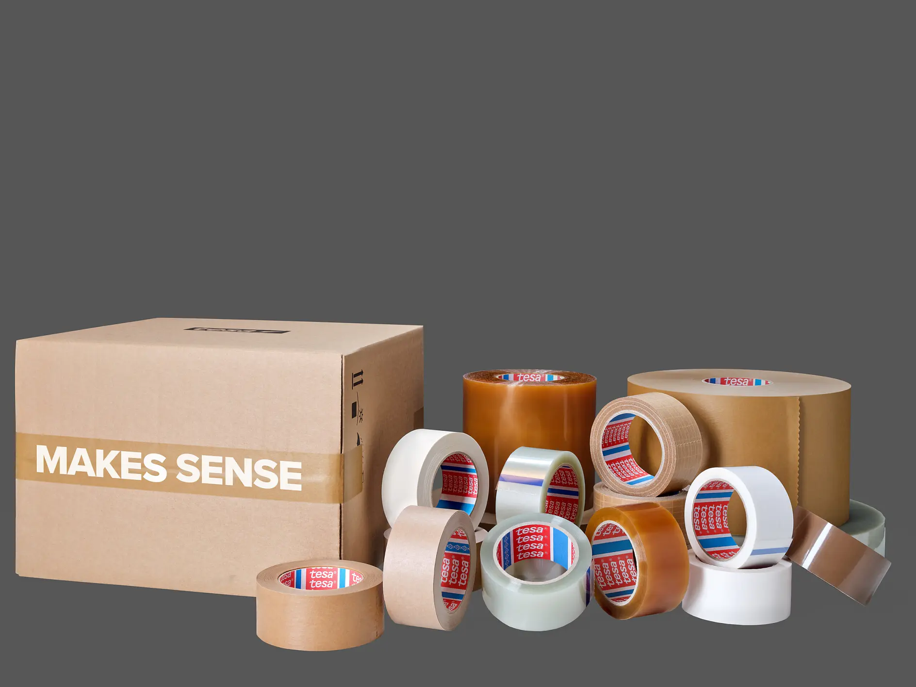 various rolls of tesa adhesive tape in different sizes and colors arranged next to a cardboard box labeled "MAKES SENSE" on a gray background