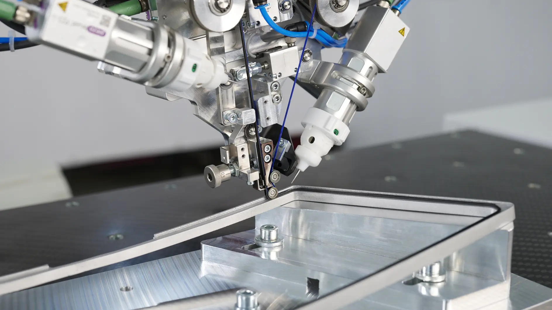 Close-up of a robotic arm with mechanical and pneumatic parts assembling a metallic piece using tesa tape on a precision workbench.
