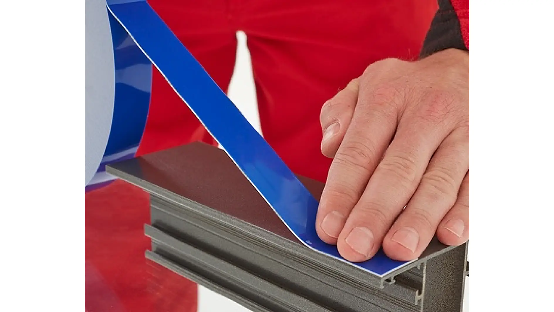 A person’s hand is applying a strip of blue tesa tape onto the edge of a rectangular metal or plastic surface against a red background. (This text has been generated by AI)