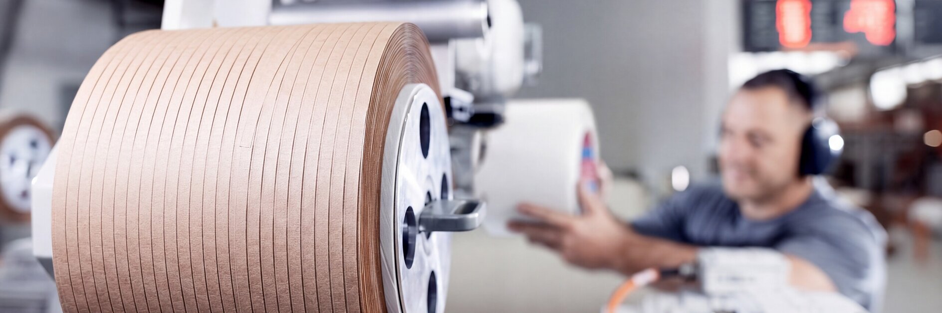 tesa branded industrial machine winding brown adhesive tape in a factory setting with a worker operating controls nearby