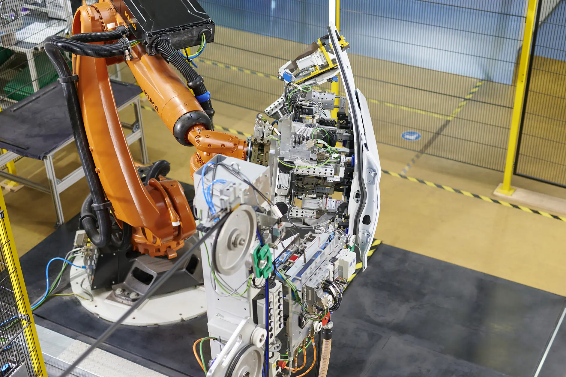 industrial robotic arm assembling electronic components on a circuit board in a factory setting with safety barriers visible tesa