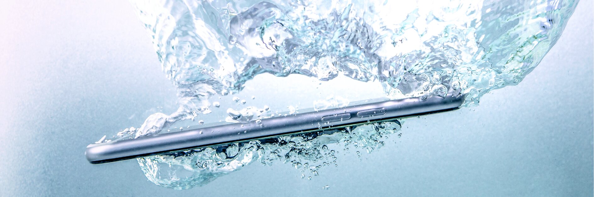 A smartphone submerged in water, creating bubbles and ripples in the surrounding liquid, is secured with tesa tape.
