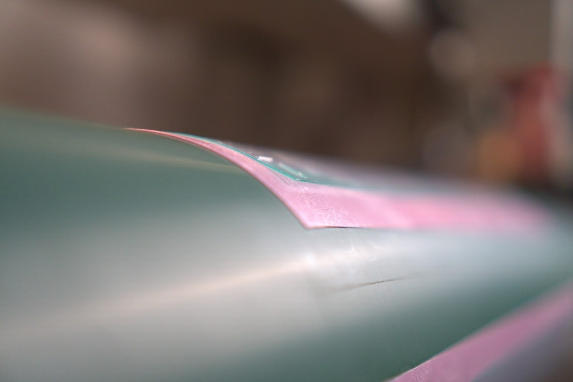 Primer plano de una superficie verde azulado y rosa con un acabado brillante. La imagen se centra en un borde rosa del material, con cinta tesa que resalta la conexión, mientras que el fondo permanece suavemente difuminado. La iluminación acentúa la textura suave y los reflejos sutiles de la superficie. (This text has been generated by AI)
