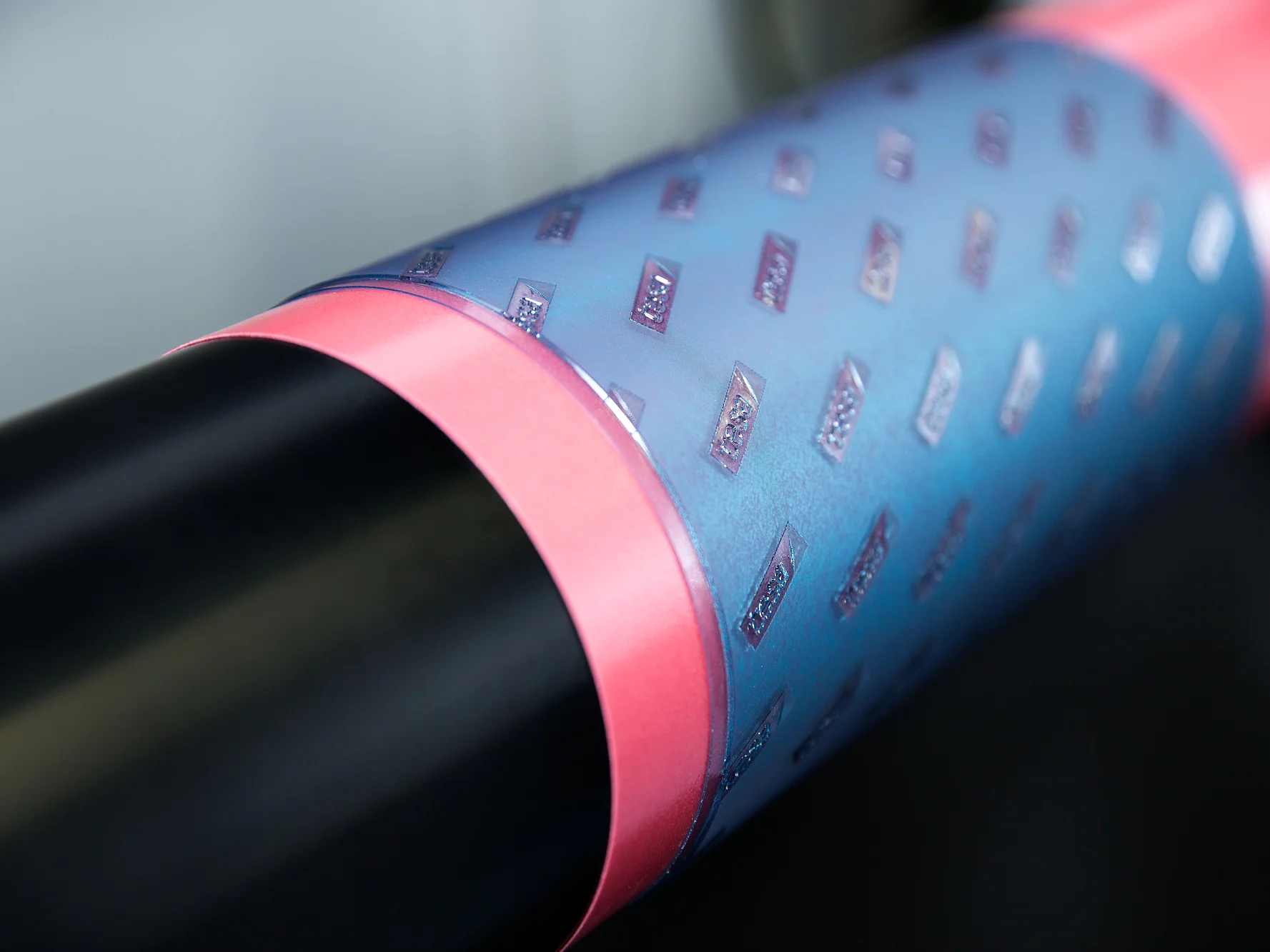 reliable-plate-adhesion-ea Vista en primer plano de un objeto cilíndrico envuelto con cinta adhesiva reflectante tesa azul y rosa. La sección azul presenta pequeños patrones en relieve. El fondo está difuminado, lo que resalta la textura y los colores de la envoltura de cinta tesa. (This text has been generated by AI)