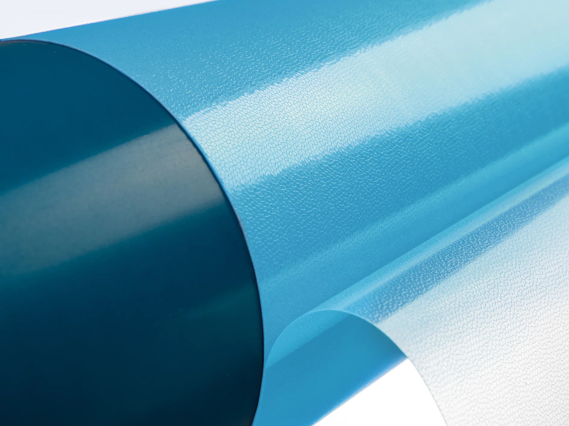 tesa-softprint-ea-flex-medium-hard-blue-on-sleeve-with-open-liner (1) Primer plano de un rollo de cinta adhesiva Tesa azul y transparente brillante parcialmente desenrollado, que muestra su textura suave. La cinta Tesa tiene una superficie reflectante y está colocada sobre un fondo blanco liso. (This text has been generated by AI)