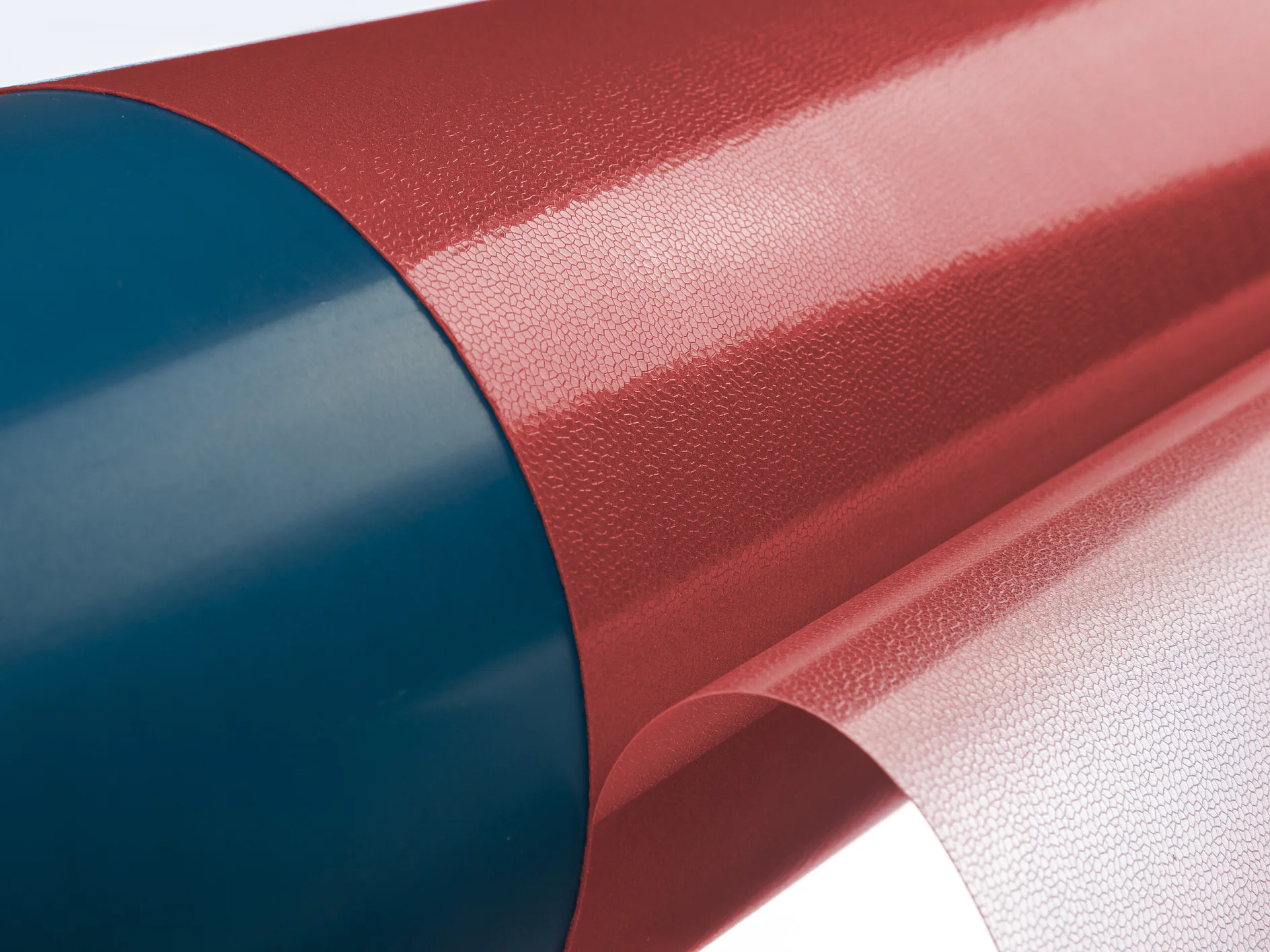tesa-softprint-ea-flex-soft-red-on-sleeve-with-open-liner (1) Primer plano de un objeto cilíndrico rojo y azul parcialmente envuelto con una lámina transparente y brillante de cinta tesa. La superficie roja tiene un aspecto texturizado. La lámina transparente de cinta tesa está parcialmente despegada, revelando la superficie roja que se encuentra debajo. (This text has been generated by AI)