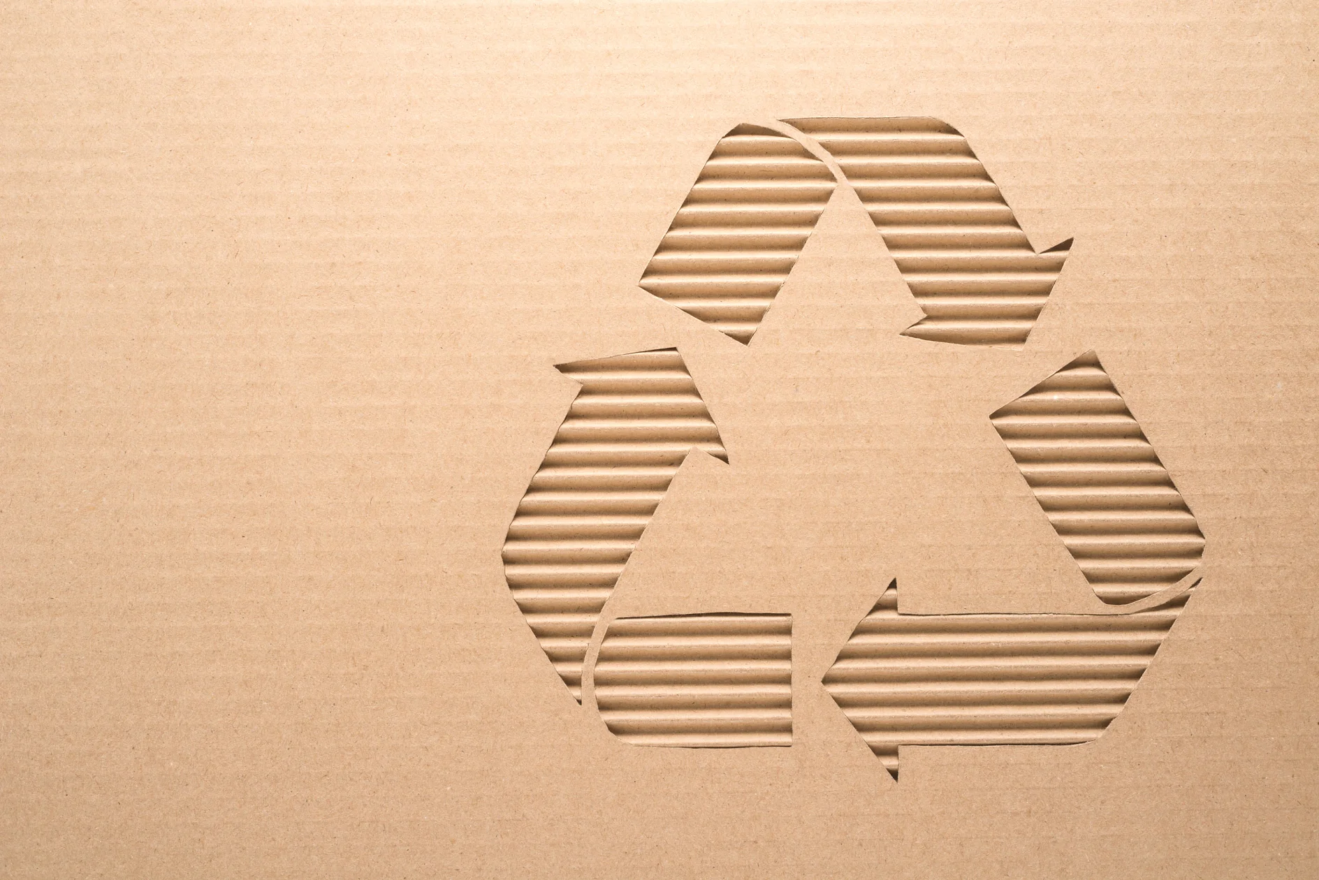 Cardboard with a cut-out recycling symbol featuring three arrows forming a triangle, representing the concept of recycling and sustainability. The surface has a corrugated texture and is secured with tesa tape. (This text has been generated by AI)