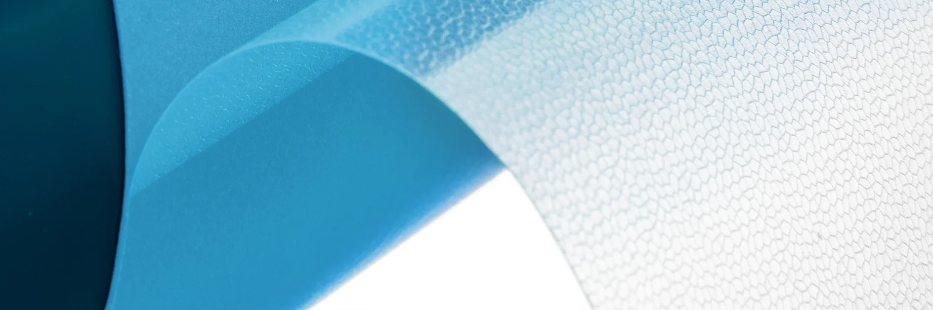 Close-up of a blue, translucent, textured plastic sheet being unrolled. The surface has a slightly pebbled pattern, and the material is shown in mid-roll, highlighting its flexibility and distinct blue hue. (This text has been generated by AI)