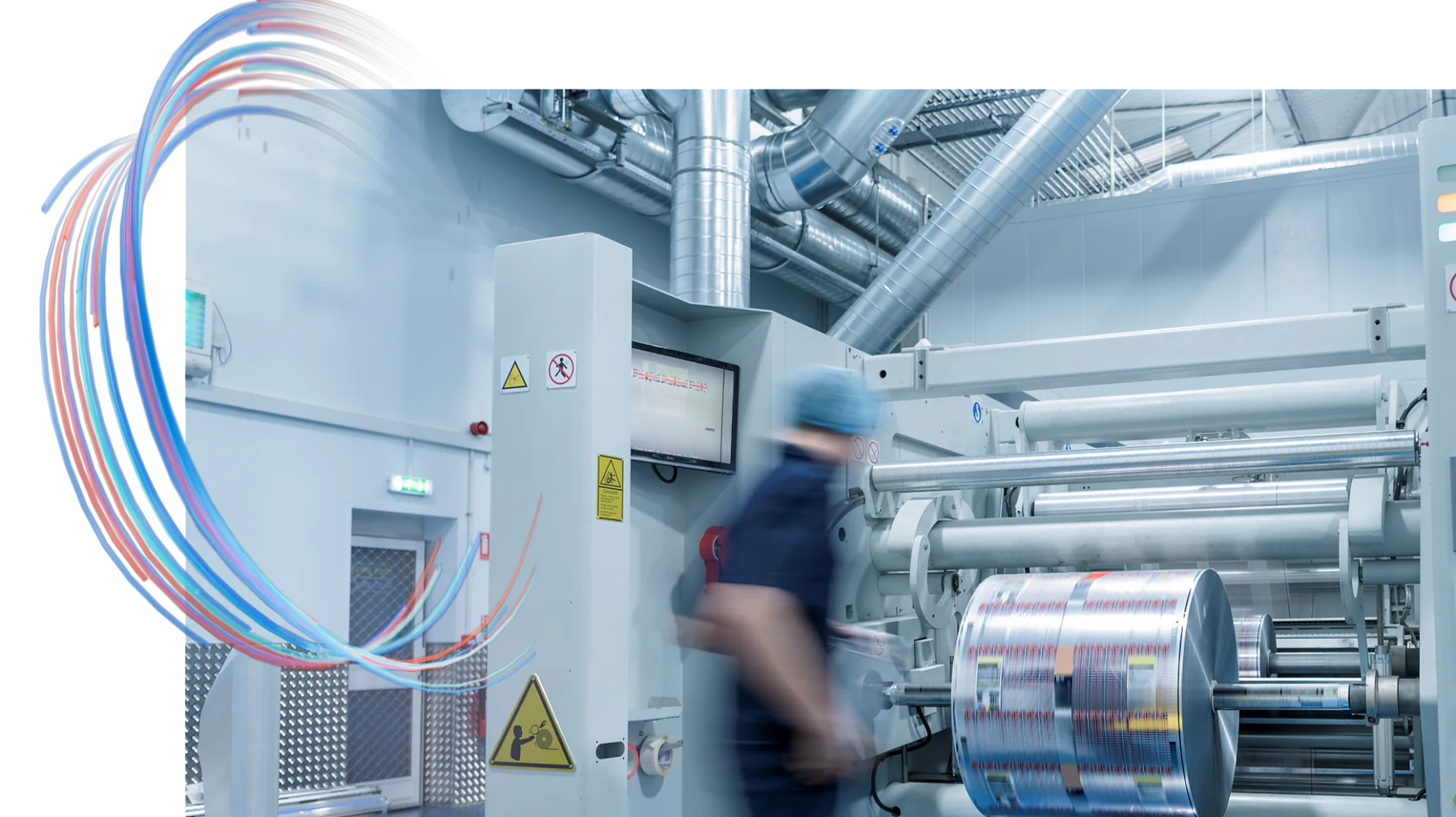 A worker in a blue uniform operates a large industrial machine in a factory setting. The machinery features metal components and a spool of printed material with tesa tape. Safety signs and a digital display are visible. Colored lines decorate the images top corner. (This text has been generated by AI)