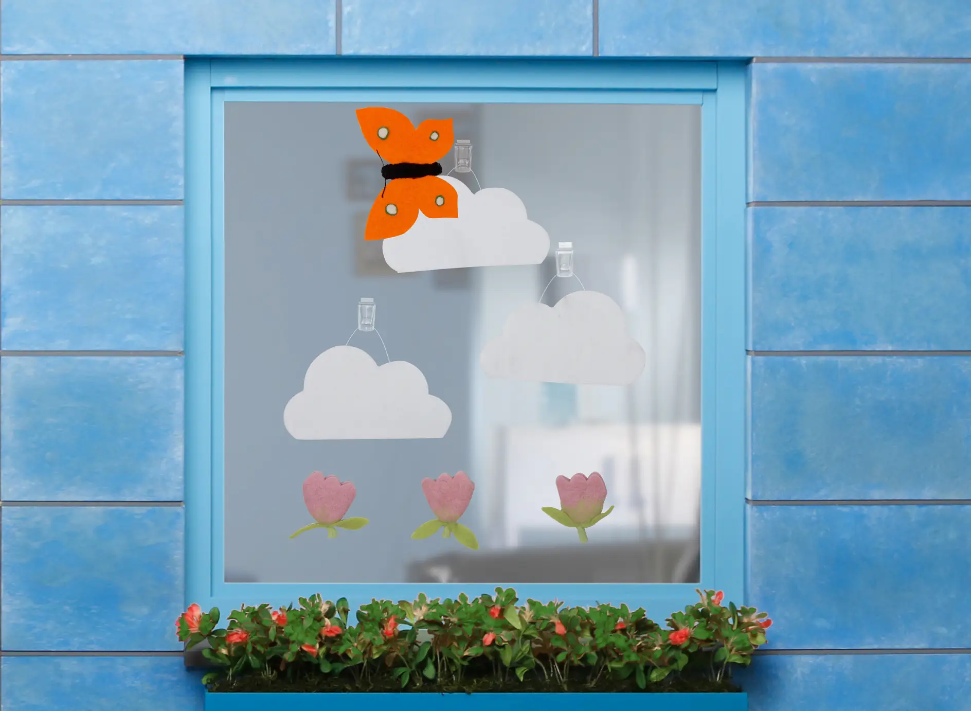 Felt clouds, butterfly and flowers fixed onto a windowpane using tesa Powerstrips® Transparent DECO Hooks LARGE and tesa Powerstrips® Strips Transparent LARGE.