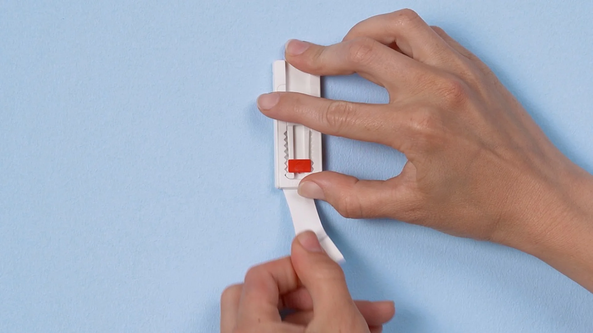 Two hands are shown using a plastic device to squeeze toothpaste from a tube against a light blue background. The device appears to have a red slider and a white body, with tesa tape making it secure and easy to use. (This text has been generated by AI)