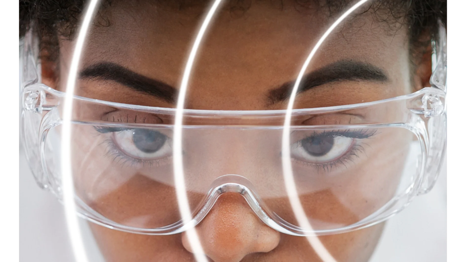 Una persona que viste una bata blanca y gafas de seguridad transparentes mira fijamente hacia adelante, rodeada de reflejos de luz circulares que crean un efecto dinámico y futurista alrededor de la cara. (This text has been generated by AI)