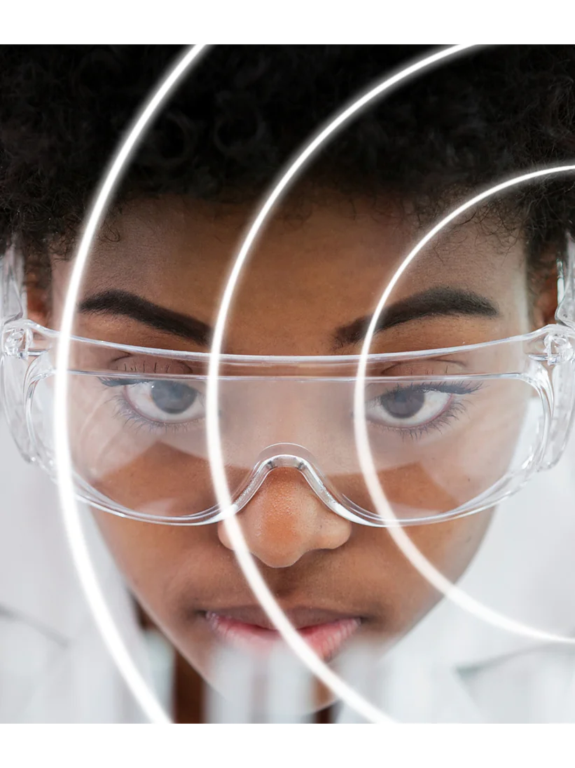 Una persona que viste una bata blanca y gafas de seguridad transparentes mira fijamente hacia adelante, rodeada de reflejos de luz circulares que crean un efecto dinámico y futurista alrededor de la cara. (This text has been generated by AI)