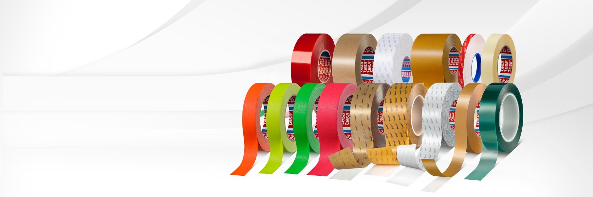 Una hilera de rollos de cinta tesa de distintos colores, diseños y materiales en posición vertical, cada uno con una sección desenrollada, sobre un fondo blanco.