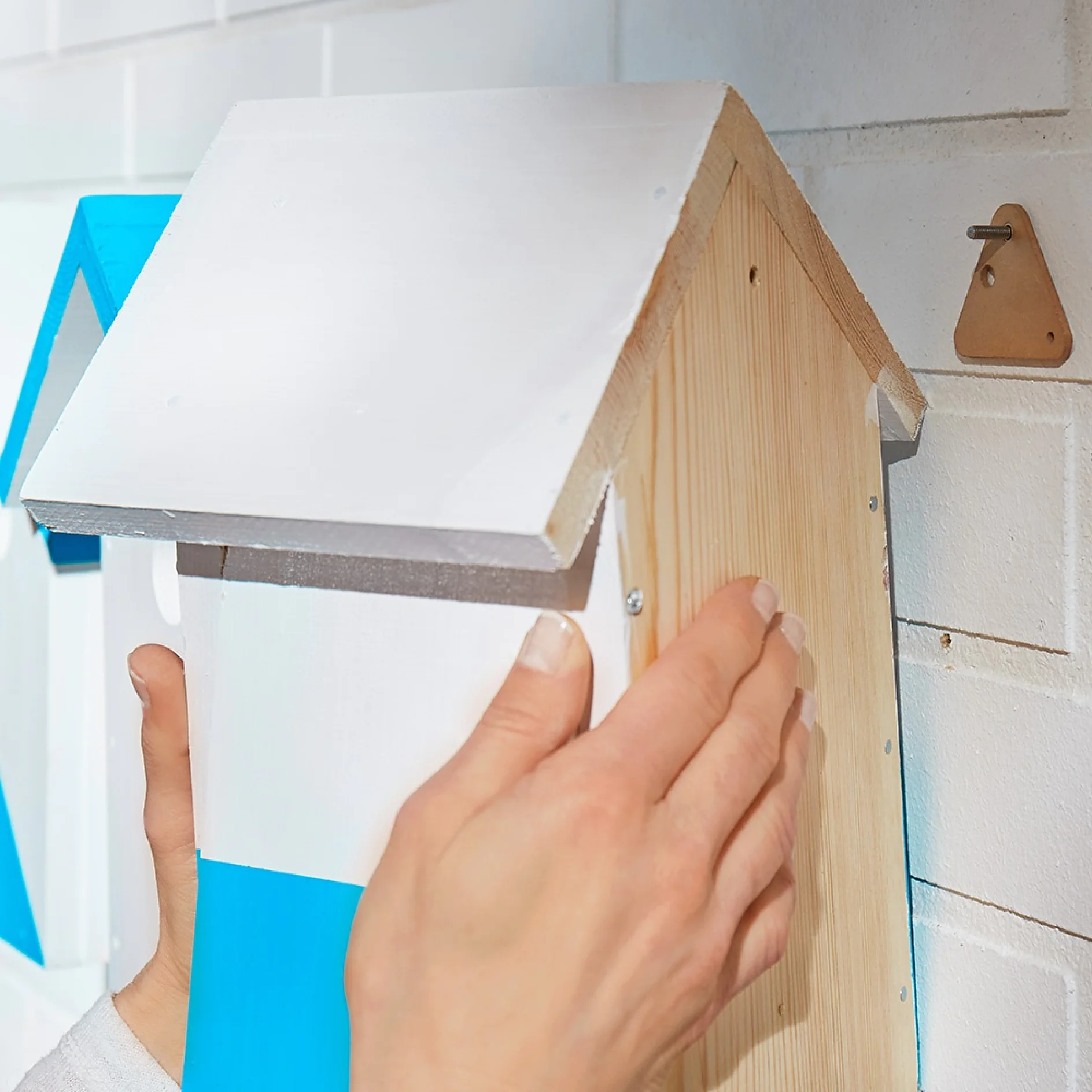 Using a tesa® Adhesive Screw Triangular for Brick & Stone 10kg to wall mount a wooden bird house.