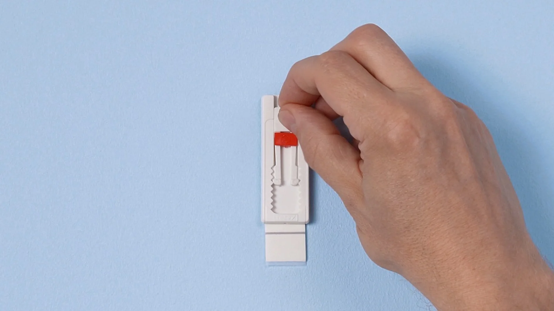 A hand is holding a small, white object with a red sliding mechanism against a blue background. The object appears to be a plastic device, possibly tesa tape or a component. (This text has been generated by AI)