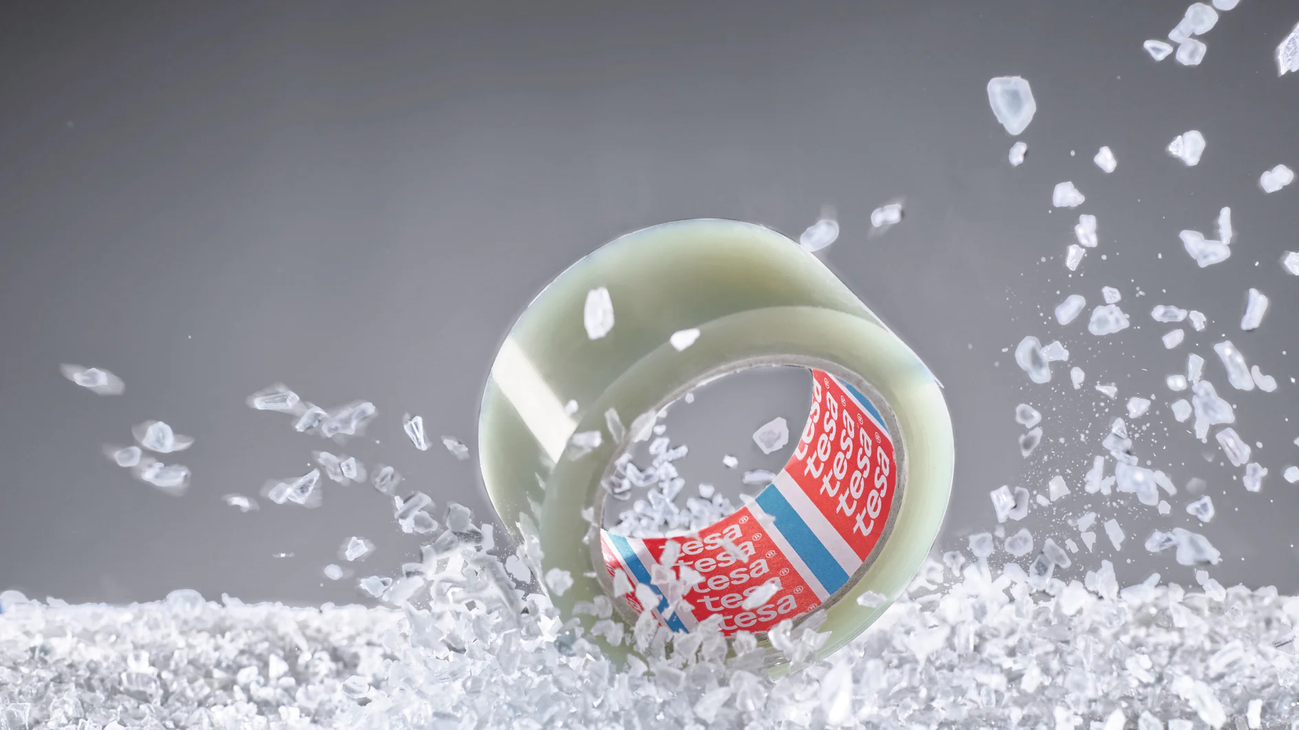 tesa adhesive tape roll suspended mid-air with scattered white packing peanuts on gray background (This text has been generated by AI)