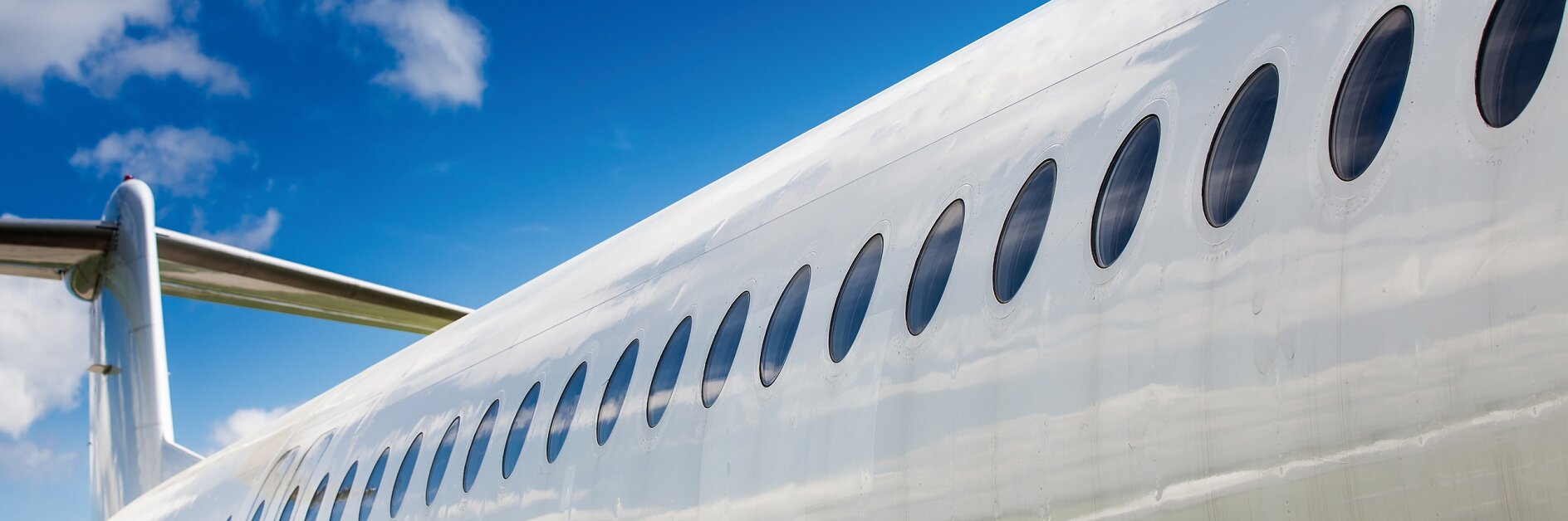 close-up of a silver airplane fuselage with oval windows under a blue sky with scattered clouds tesa