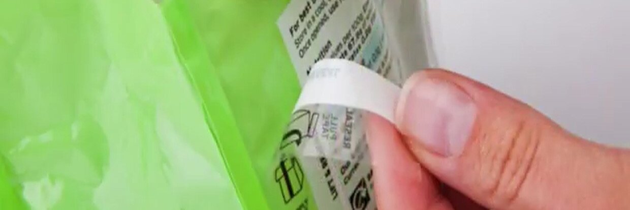 Una mano está despegando una tira resellable de una bolsa de plástico verde. El texto de la tira incluye las palabras cierre con cinta tesa resellable. Hay otros textos e íconos en la bolsa, pero no son claramente legibles. (This text has been generated by AI)