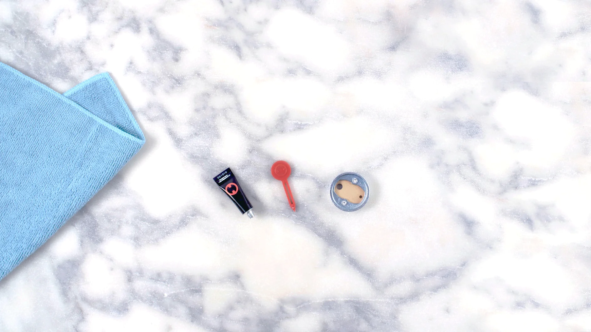 A flat-lay image shows a blue mat, a small black flashlight, a red keychain flashlight, and a round silver and beige item on a marble surface. The edges of the mat are secured using tesa tape. (This text has been generated by AI)