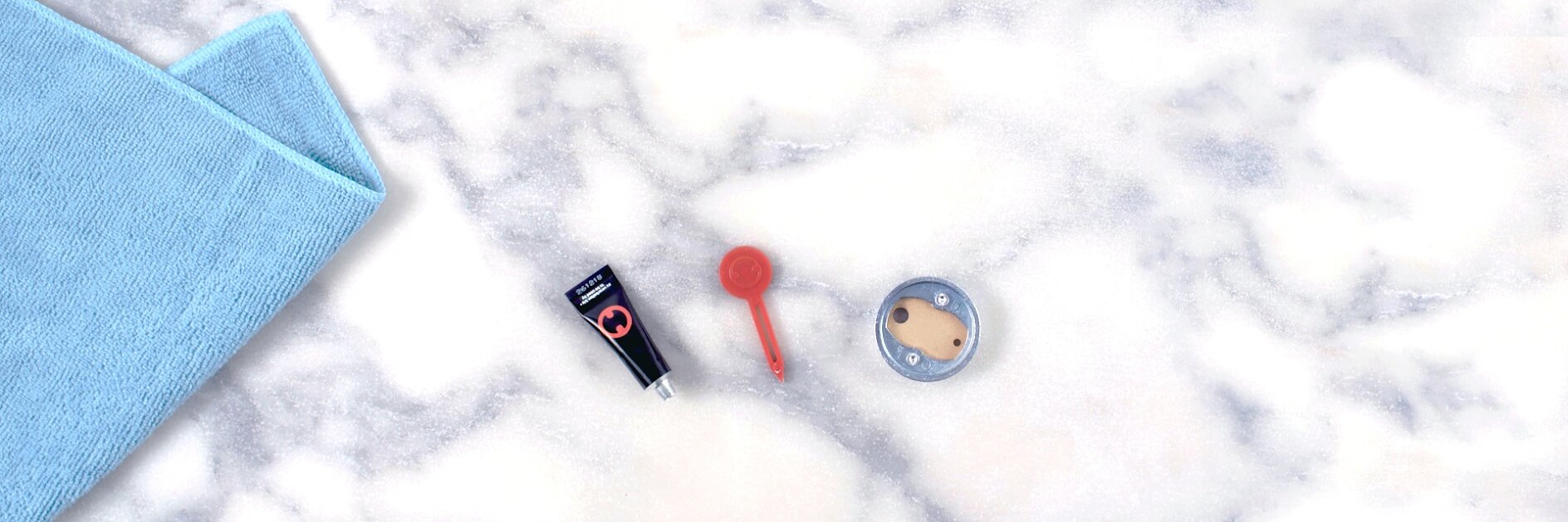 A flat-lay image shows a blue mat, a small black flashlight, a red keychain flashlight, and a round silver and beige item on a marble surface. The edges of the mat are secured using tesa tape. (This text has been generated by AI)