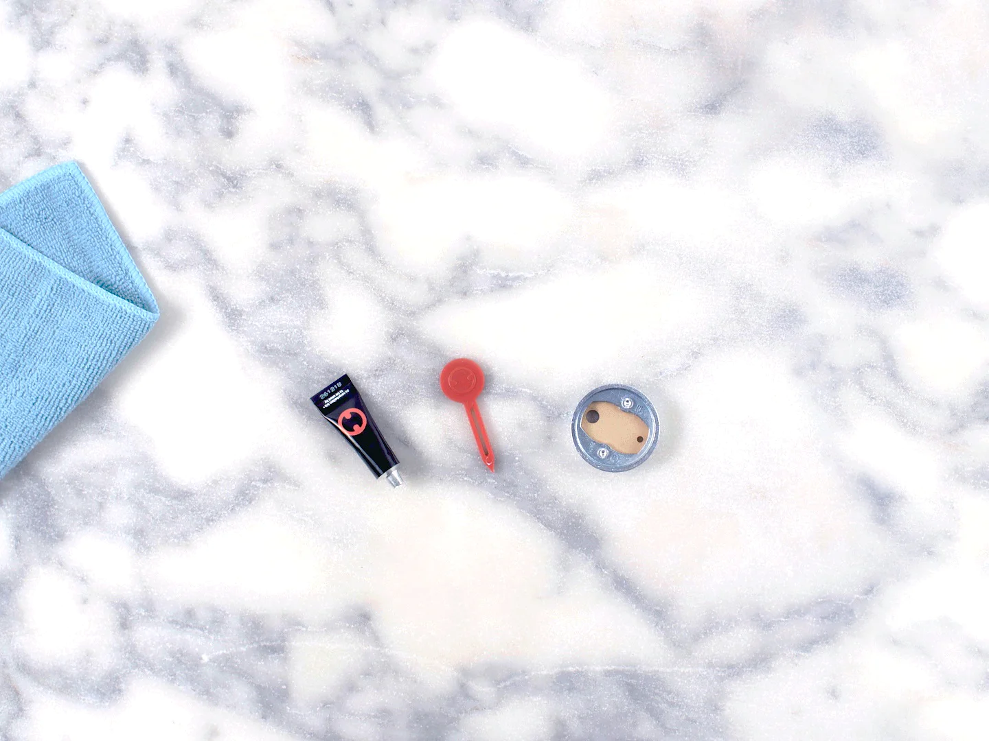 A flat-lay image shows a blue mat, a small black flashlight, a red keychain flashlight, and a round silver and beige item on a marble surface. The edges of the mat are secured using tesa tape. (This text has been generated by AI)