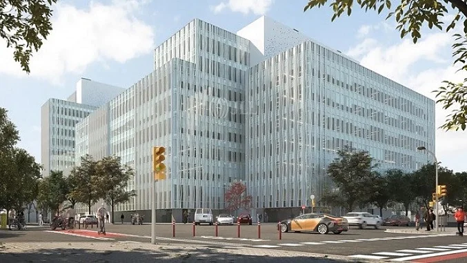 oficina-tesa-barcelona Un edificio moderno de vidrio de varios pisos en la esquina de una calle de la ciudad. La estructura tiene una fachada en forma de cuadrícula con paneles reflectantes. En primer plano se ven árboles, peatones y algunos automóviles. El cielo está parcialmente nublado y se ven semáforos. (This text has been generated by AI)