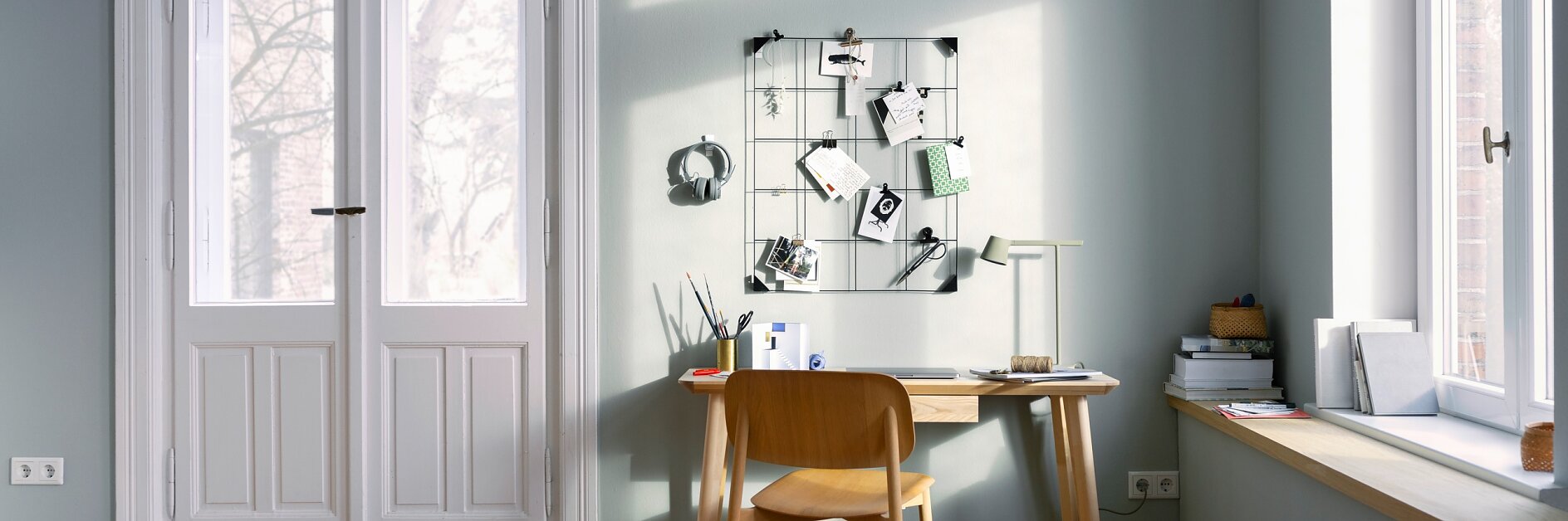 Home-Office-Soluciones - Imagen destacada: Un escritorio está colocado junto a una pared con un panel organizador de utensilios.
