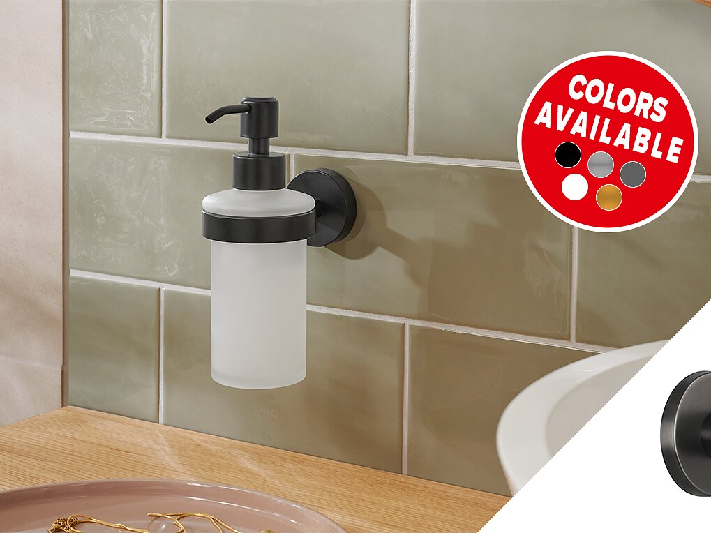 Un dispensador de jabón montado en la pared con una botella esmerilada y una bomba negra se fija a una pared de azulejos verde claro con cinta tesa. Una calcomanía circular muestra varios colores disponibles: rojo, blanco, gris, beige y negro. En primer plano hay un mostrador de madera. (This text has been generated by AI)