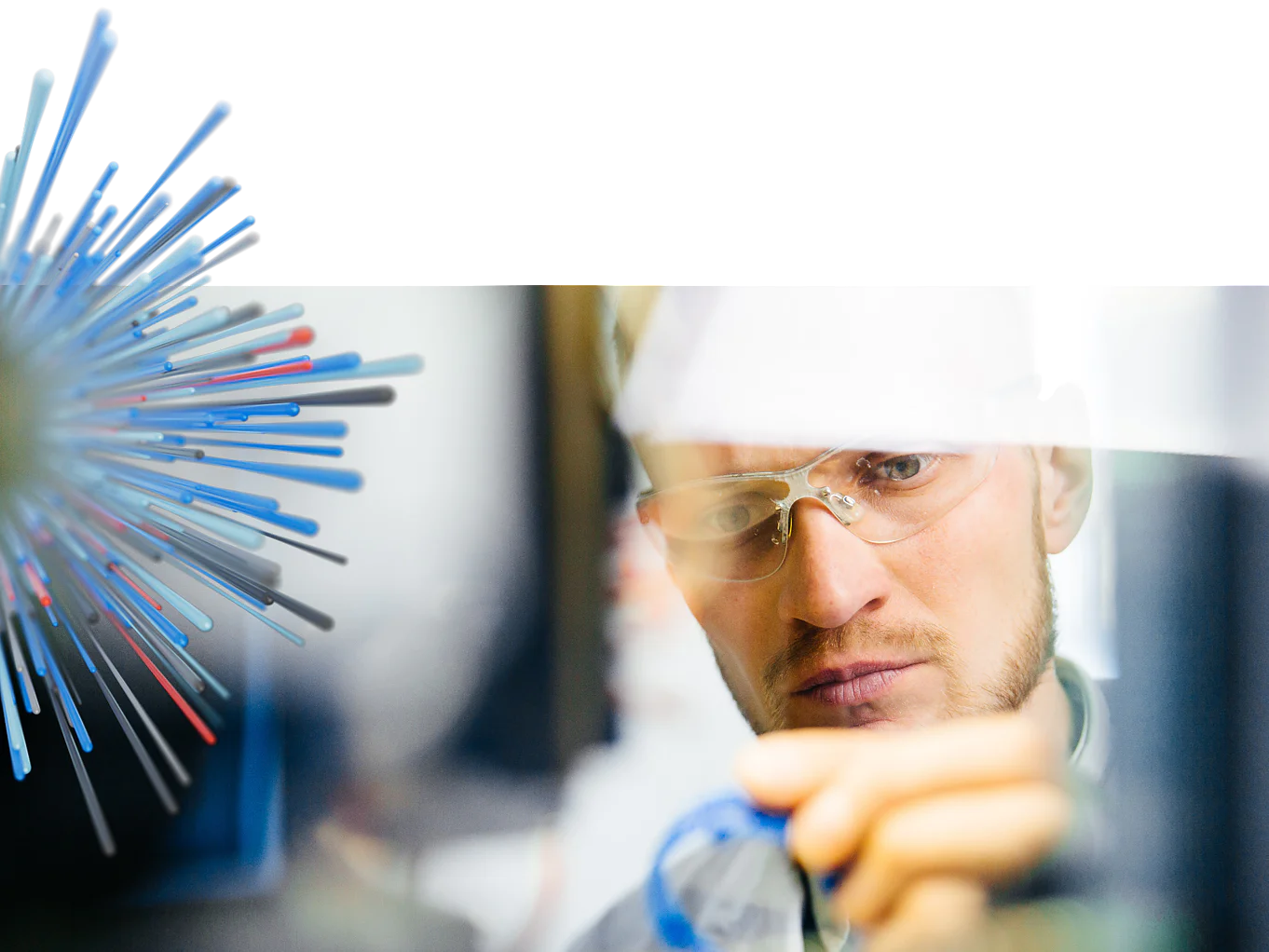 A man wearing safety glasses is focused on a task, holding a small blue object. A digital graphic resembling a burst of lines in various shades intersects the image, alluding to the effectiveness of tesa tape in various settings. (This text has been generated by AI)