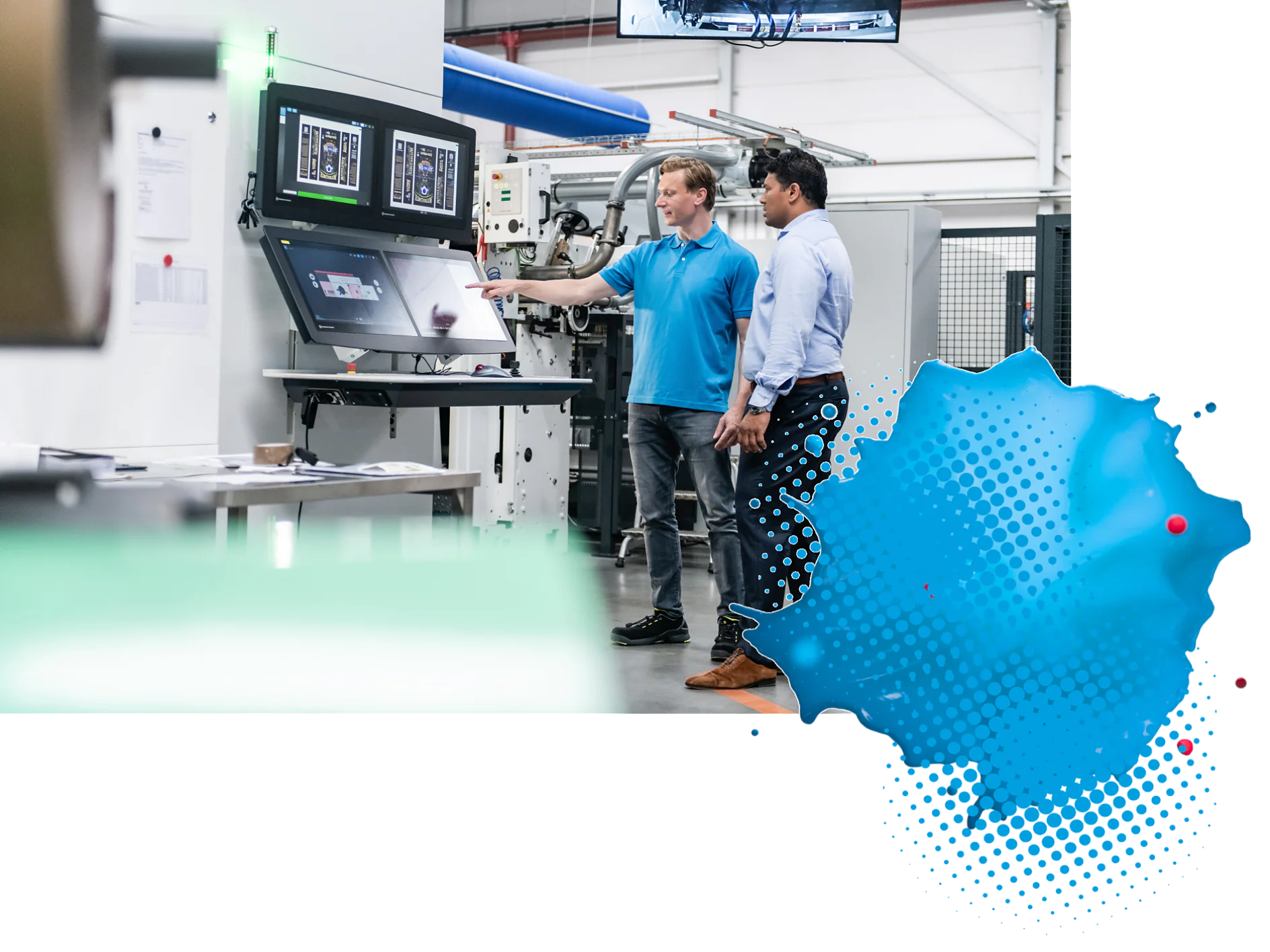 Two people stand in front of a large computer monitor in an industrial setting. One person points at the screen displaying technical diagrams. Machinery is visible in the background. There is a blue abstract shape at the bottom right corner, where tesa tape products are likely being used to enhance functionality and performance. (This text has been generated by AI)