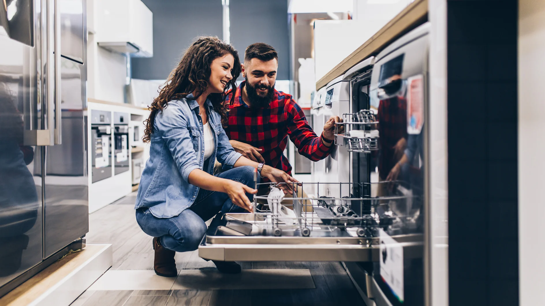 Beautiful and happy young couple buying dishwasher in modern appliances store.