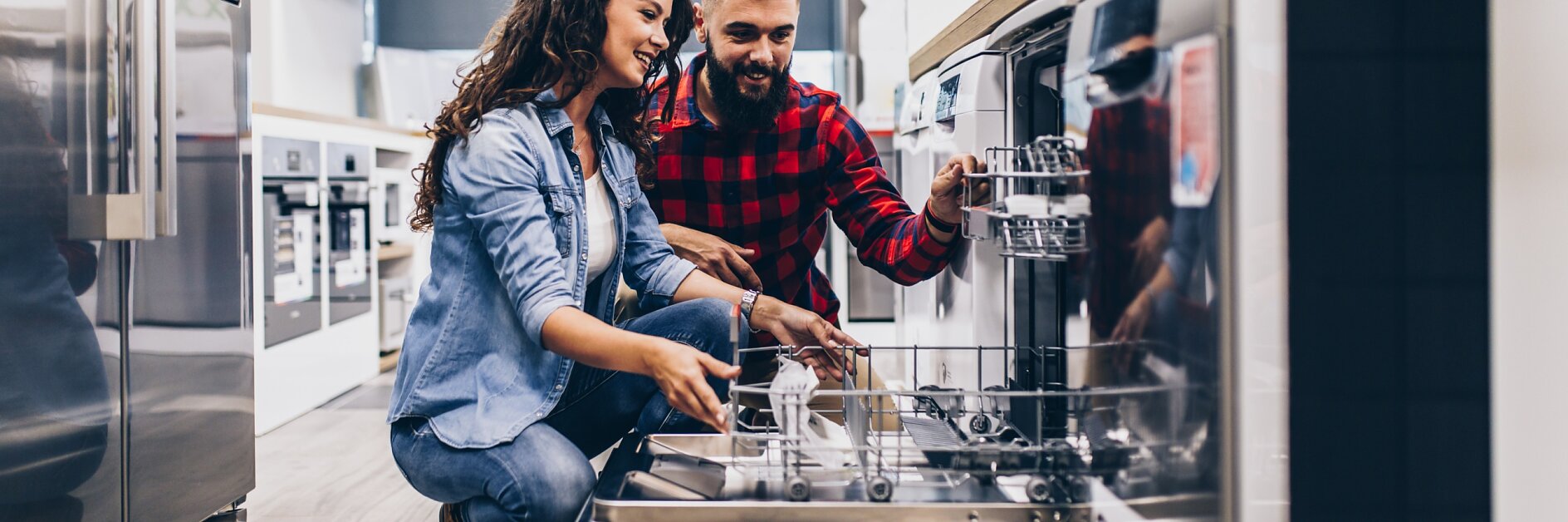 Beautiful and happy young couple buying dishwasher in modern appliances store.