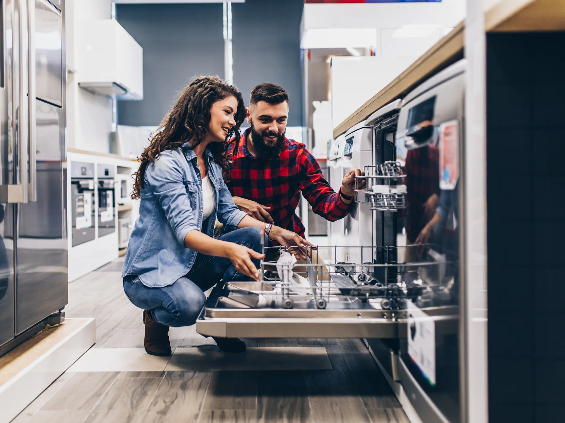 Beautiful and happy young couple buying dishwasher in modern appliances store.