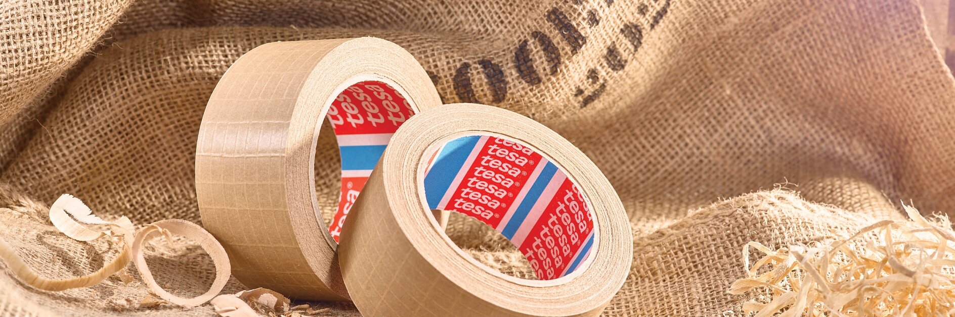 two rolls of tesa adhesive tape on burlap fabric with wood shavings and straw in a rustic indoor setting
