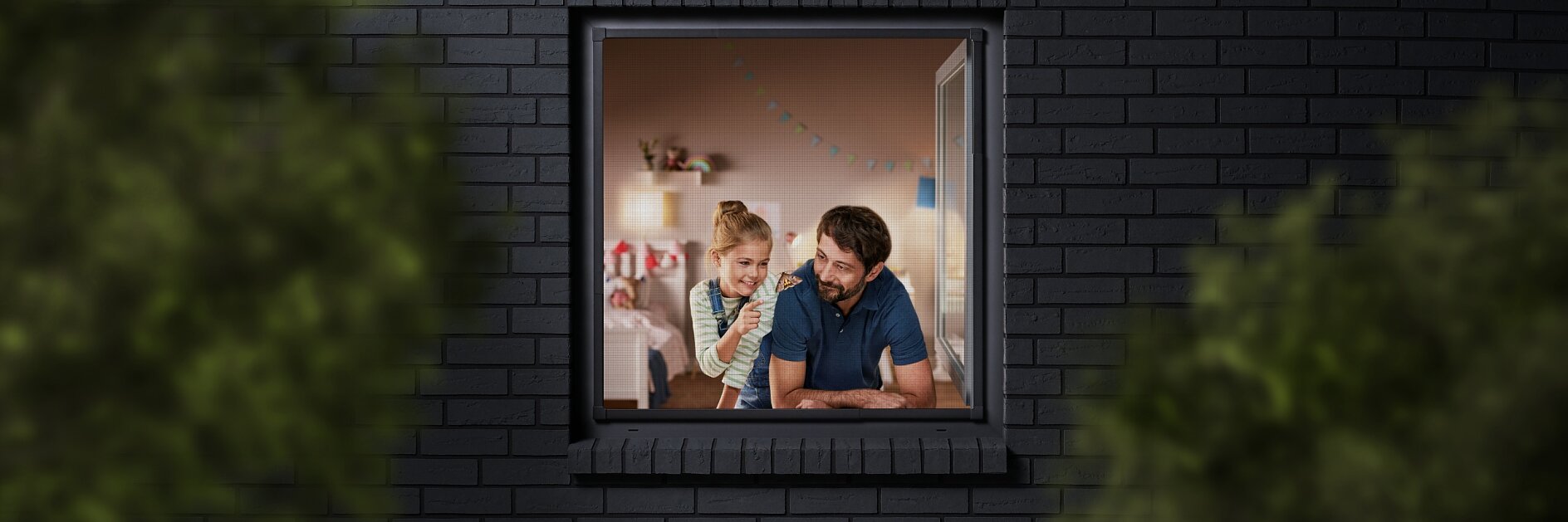 A man and a child are seen through a window, looking into a room decorated with colorful bunting. The building has dark brick walls, and the view is partially framed by blurred greenery. The man is wearing a blue shirt, and the child is sitting beside him. (This text has been generated by AI)