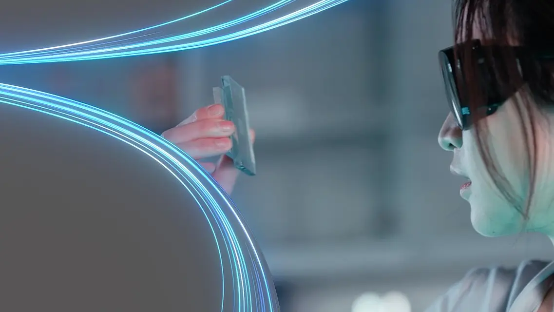 A person wearing glasses closely examines a small electronic device in their hand, using tesa tape. Blue and white light streaks curve across the image, adding a dynamic effect. The background is a soft-focus indoor setting. (This text has been generated by AI)