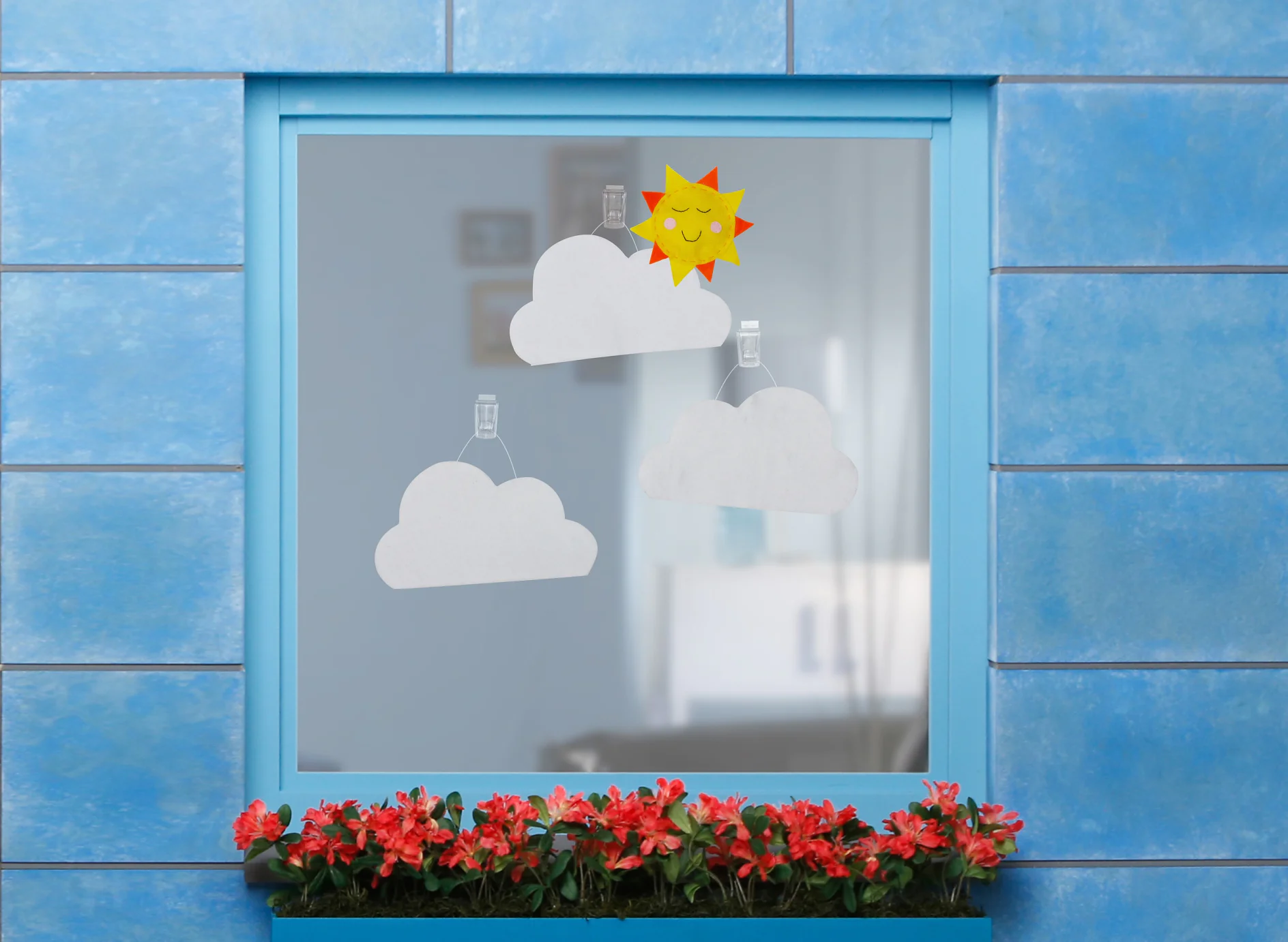 Felt clouds and a felt sun fixed onto a windowpane using tesa Powerstrips® Transparent DECO Hooks LARGE and tesa Powerstrips® Strips Transparent LARGE.