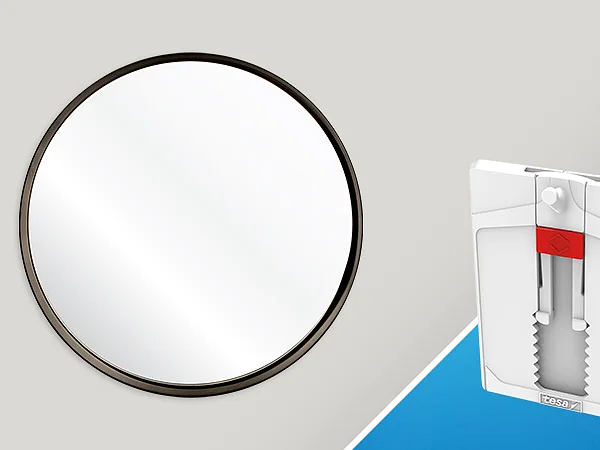 A round mirror with a black frame is on the left. On the right, a white wall anchor with a red component is shown against a blue and gray background, secured using tesa tape. (This text has been generated by AI)