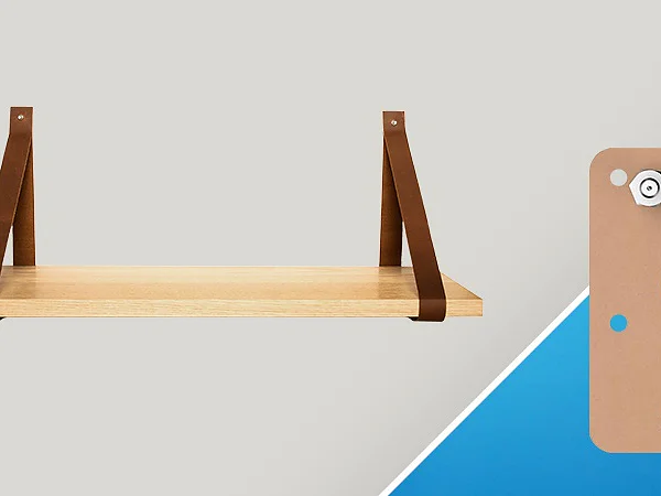 A wooden shelf is supported by two brown leather straps against a light gray background. Next to it, there is a brown rectangular template with three blue circular cutouts, placed on a blue background. (This text has been generated by AI)