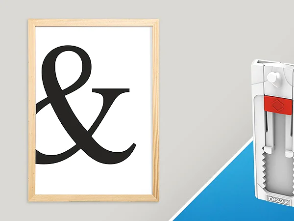 A framed artwork featuring a large black ampersand symbol on a white background is displayed alongside a white wall hanger product with a red accent, placed on a blue and white diagonal backdrop. tesa tape was used in the setup of this display. (This text has been generated by AI)