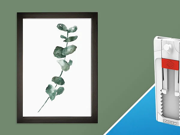 A framed watercolor painting of a eucalyptus branch on a green background is displayed on the left. To the right, a white and red tesa tape adhesive wall hanger on a blue background is shown in diagonal split view. (This text has been generated by AI)