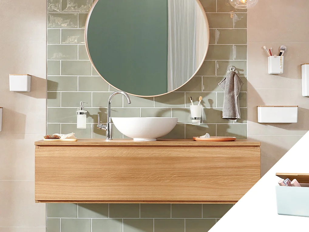 A modern bathroom features a wooden vanity with a white vessel sink, a round mirror, and green subway tiles. Various white wall-mounted accessories hold toiletries securely with tesa tape. An inset shows a white box with a wooden lid containing small items neatly held in place by tesa tape. (This text has been generated by AI)