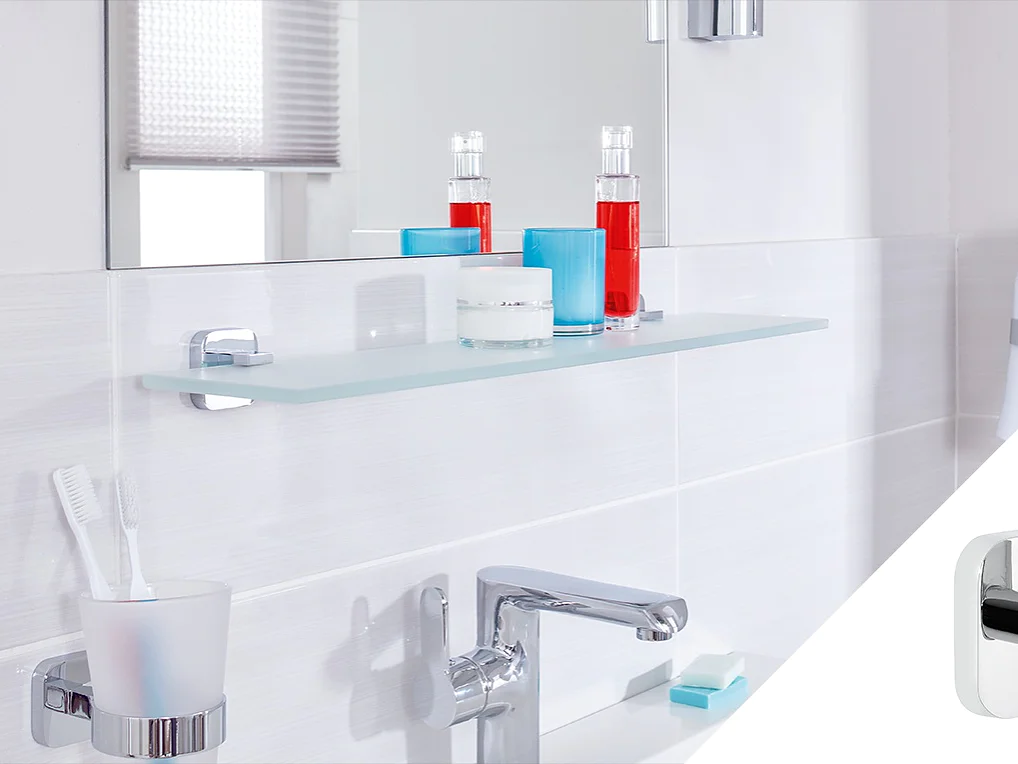 A modern bathroom features a silver faucet and a glass shelf with items on it, including red and blue bottles and a white candle. A toothbrush holder with two toothbrushes is on the counter. A chrome accessory is shown in a small inset on the right, held securely using tesa tape. (This text has been generated by AI)