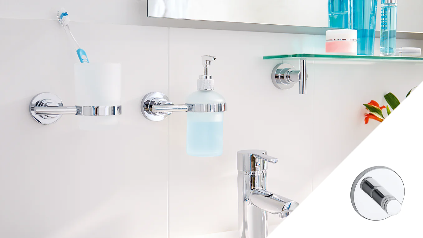 Bathroom scene with a chrome toothbrush holder, liquid soap dispenser, and faucet. Holding toiletries is a glass shelf that features a pink jar. The backdrop is a white tile setting, complemented by a partially visible plant adorned with orange flowers. An inset highlights a magnified chrome detail secured using tesa tape. (This text has been generated by AI)