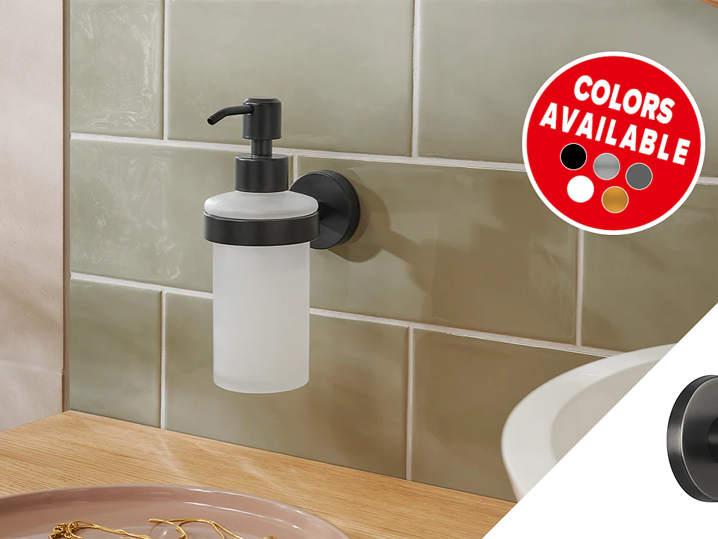 A wall-mounted soap dispenser with a frosted bottle and black pump is attached to a light green tiled wall using tesa tape. A circular decal shows various available colors: red, white, gray, beige, and black. A wooden counter is in the foreground. (This text has been generated by AI)