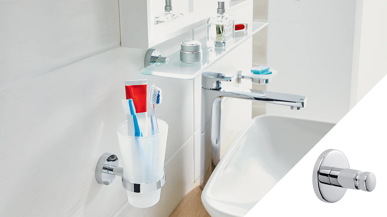 A bathroom sink area features a white cup holding toothbrushes and toothpaste mounted on the wall using tesa tape. Above, a shelf holds toiletries. A silver faucet is attached to the sink. On the right, a silver wall hook is shown. (This text has been generated by AI)