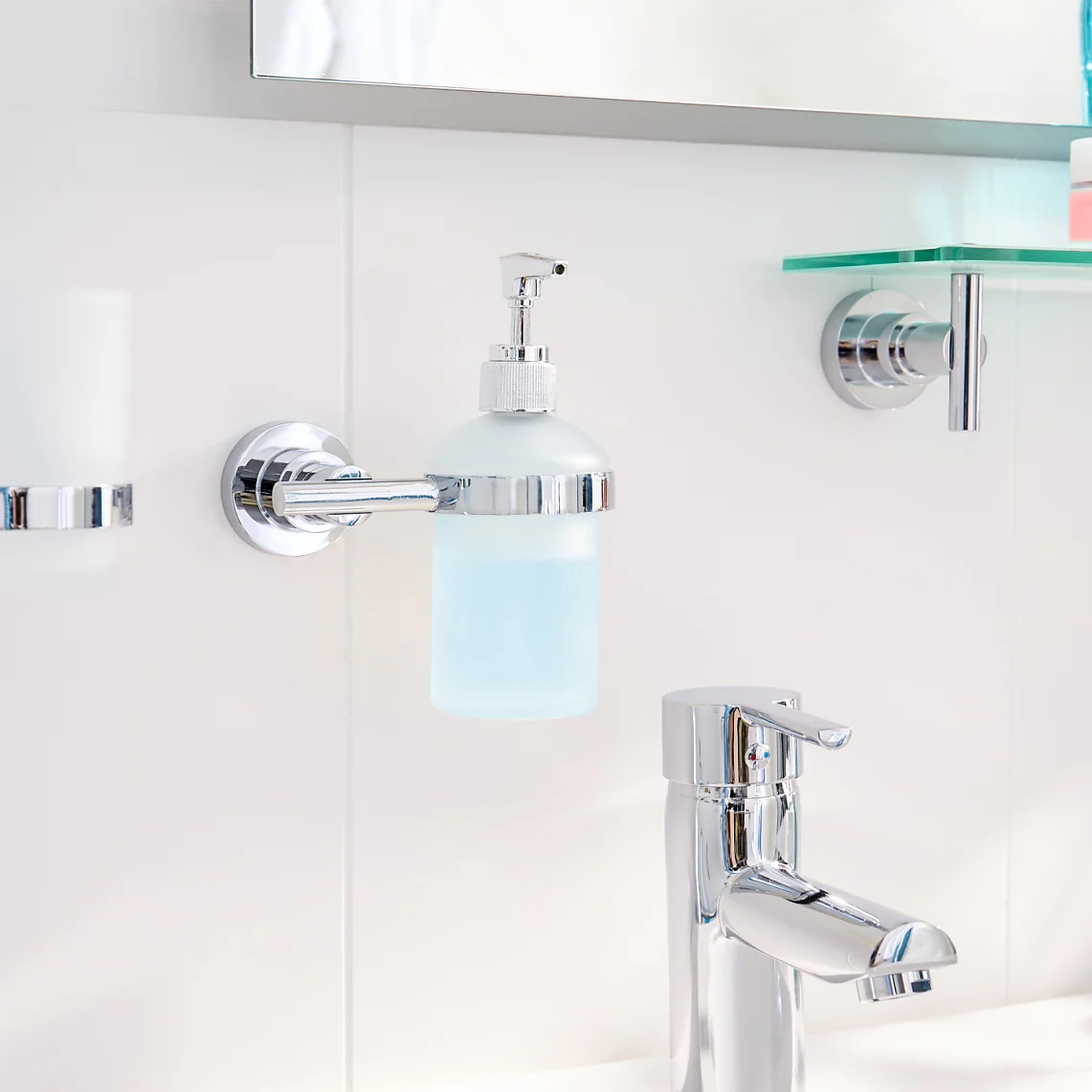 In the bathroom sink area, a chrome faucet complements a white counter. A toothbrush and holder, along with a soap dispenser, are securely mounted using tesa tape on the tiled wall. A shelf holding toiletries is also affixed with tesa tape. On the right side of the counter sits a small blue vase filled with orange flowers. (This text has been generated by AI)